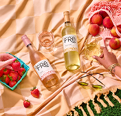 Bird's eye view of two bottles of FRE Alcohol-Removed wine on a peach colored picnic blanket with strawberries and peaches