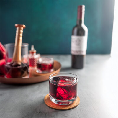 closeup of a deep red mocktail with a bottle of FRE Alcohol-Removed Cabernet Sauvignon in the background