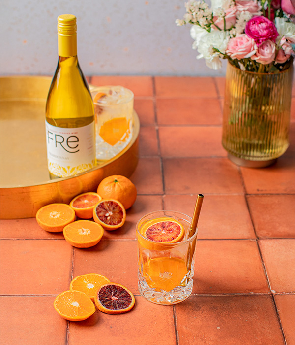 Glass of citrus breeze mocktail with slices of orange and a bottle of Fre non-alcoholic chardonnay white wine in the background