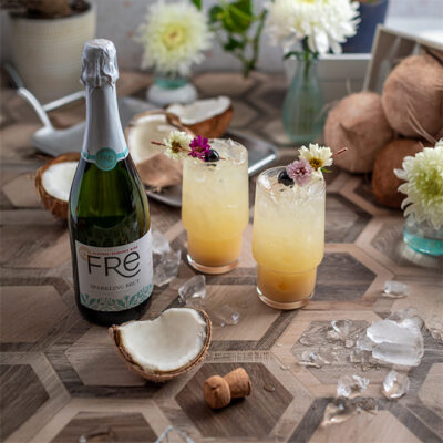 color image of a bottle of FRE Alcohol-Removed Sparkling Brut with two cocktails on a table with flowers