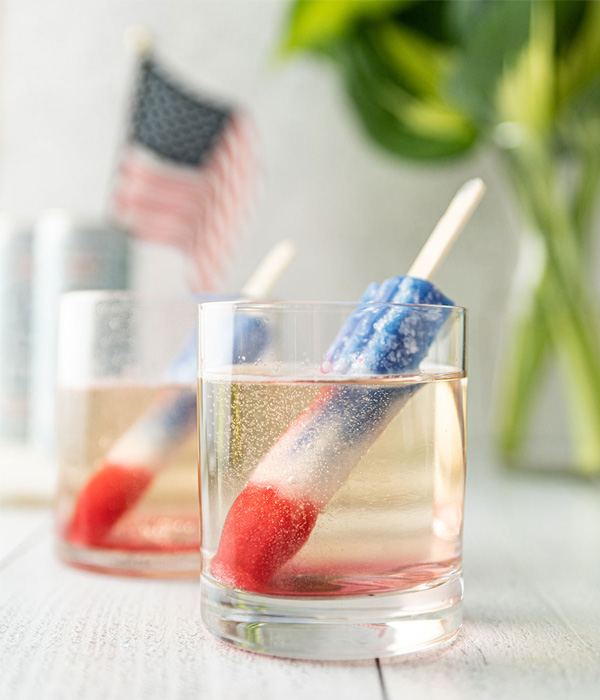 color image of 2 glasses of FRE Alcohol-Removed Sparkling Brut with a red, white, and blue popsicle in the liquid
