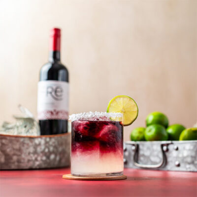 color image of a bottle of FRE Alcohol-Removed wine with a dark red and white cocktail with a lime wheel garnish