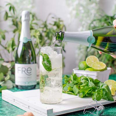 brightly colored image of a tall effervescent mocktail next to a bottle of FRE Alcohol-Removed Sparkling Brut