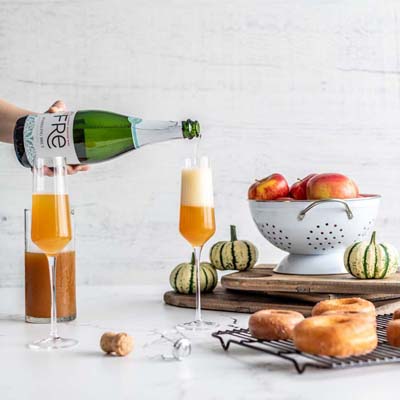 Color photo of a bottle of FRE Alcohol-Removed Sparkling Brut pouring into a champagne flute with apple garnishes in the background