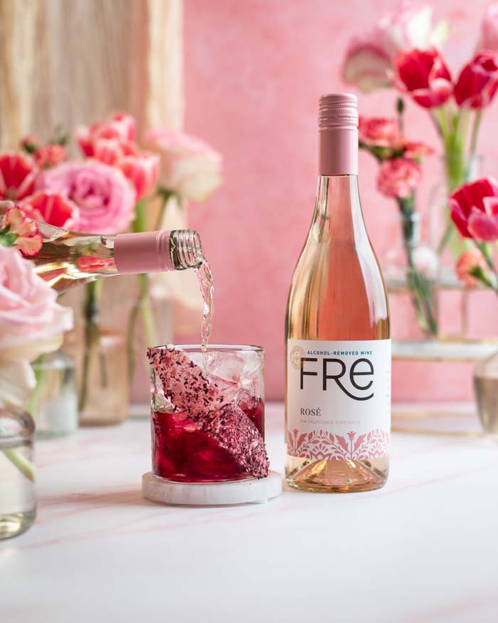 color image pink flowers in the background with a bottle of FRE Alcohol-Removed Rose wine with a hot pink cocktail with candy rim