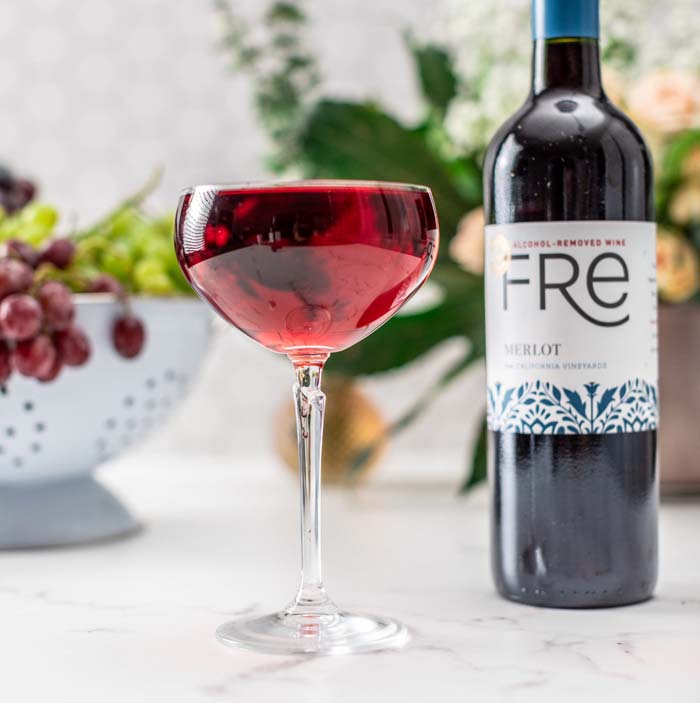 color image of a deep red mocktail with a bottle of FRE Alcohol-Removed Merlot in the background