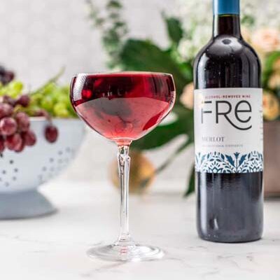 color image of a deep red mocktail with a bottle of FRE Alcohol-Removed Merlot in the background