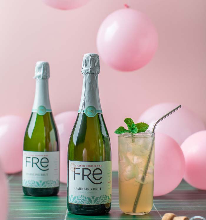 Two bottle of FRE Alcohol-Removed Sparkling Brut next to a mocktail with pink balloons in the background