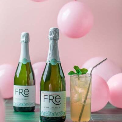 Two bottle of FRE Alcohol-Removed Sparkling Brut next to a mocktail with pink balloons in the background