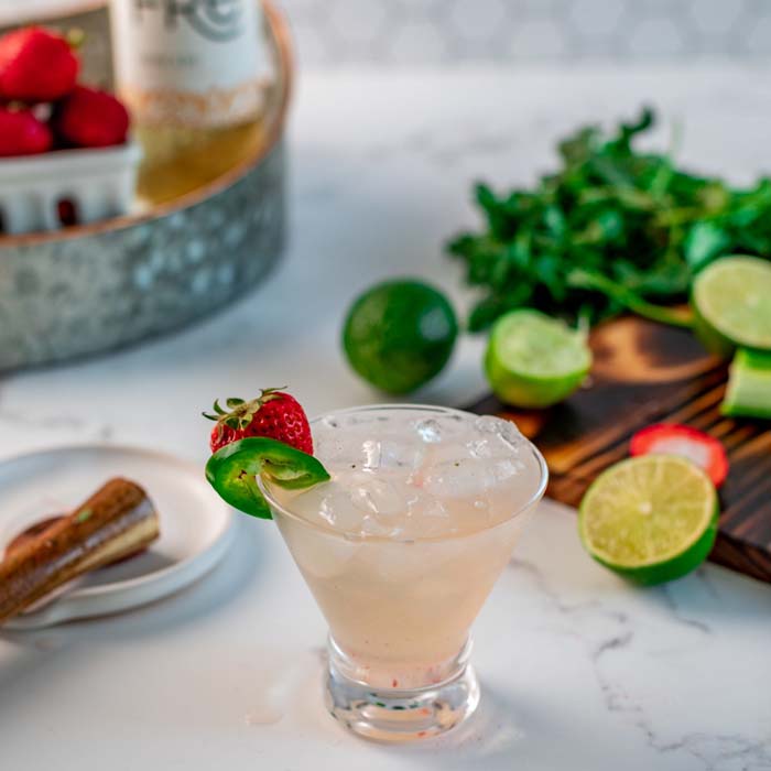color photo of a light pink cocktail with fruit garnishes in the background