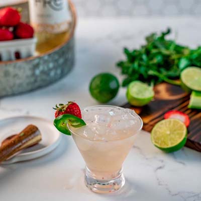 color photo of a light pink cocktail with fruit garnishes in the background