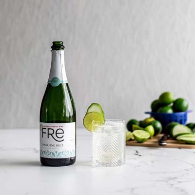 A bottle of FRE Alcohol-Removed Sparkling Brut next to a clear cocktail with lime garnishes