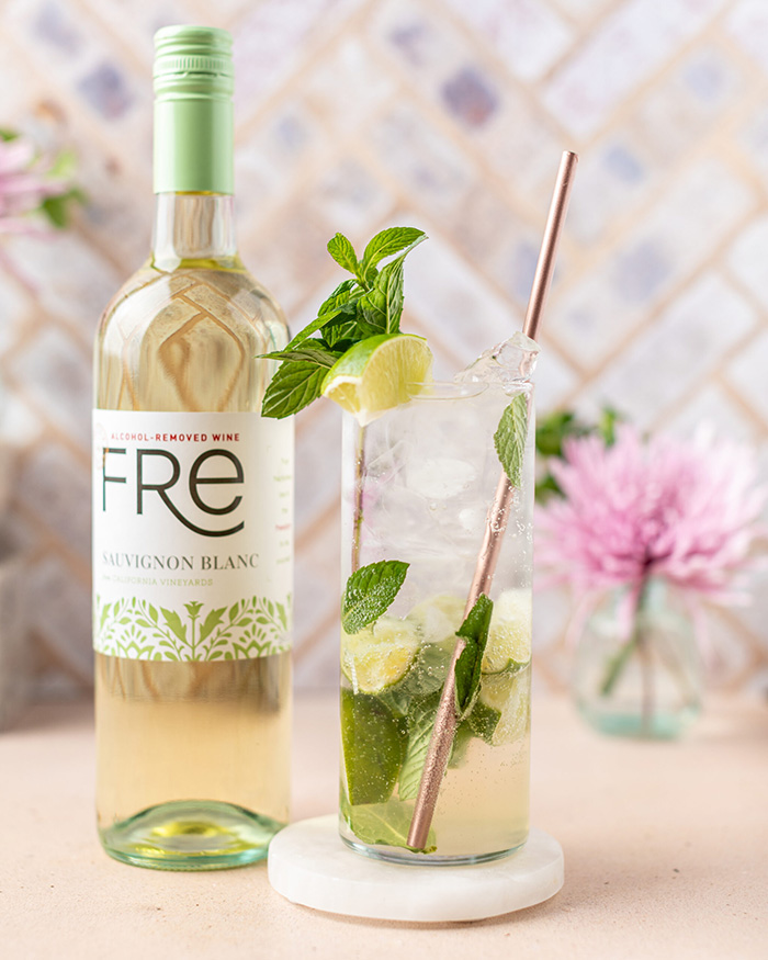 color image of a bottle of FRE Alcohol-Removed white wine with a tall glass cocktail and a pink flower