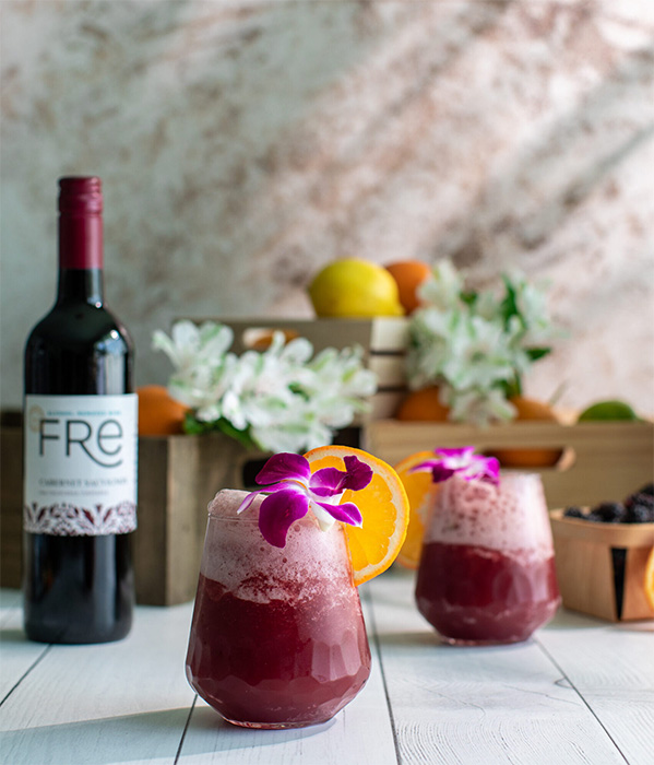 color photo of 2 red slushie mocktails with a flower garnish and bottle of FRE Alcohol-Removed Cabernet Sauvignon in the background