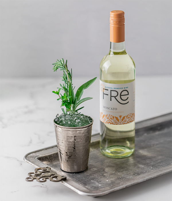 color photo of a bottle of FRE Alcohol-Removed Moscato next to a cocktail with an herb sprig garnish