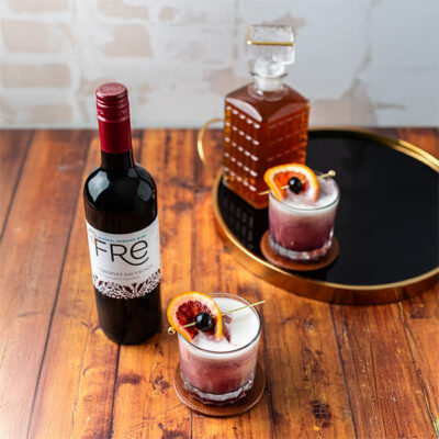 A bottle of FRE Alcohol-Removed red wine with 2 cocktails on a wood table