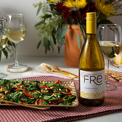Plate of Stir-Fried Spinach with Garlic and Peanuts on a plate decorated with gourds and flowers, beside glasses and a bottle of FRE alcohol-removed Chardonnay white wine