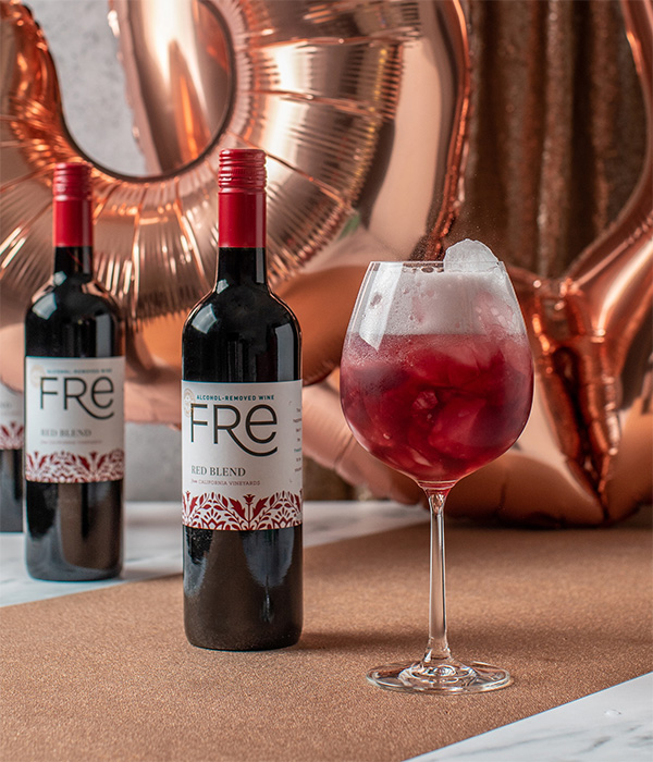 A bright red mocktail in front of two bottles of FRE Alcohol-Removed Red Blend