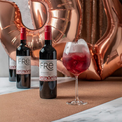 A bright red mocktail in front of two bottles of FRE Alcohol-Removed Red Blend