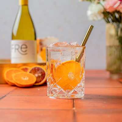 Glass of citrus breeze mocktail with slices of orange and a bottle of Fre non-alcoholic chardonnay white wine in the background