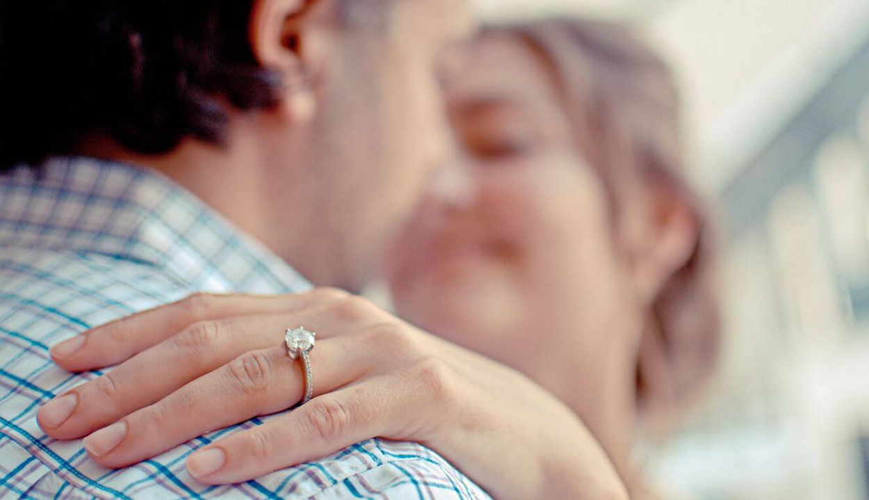 Close up of woman's hand wearing wedding ring on a man's shoulder seen from behind