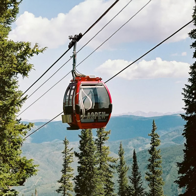 A ski gondola on wires with pine trees and mountains in the distance