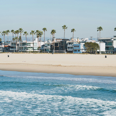 A California shoreline and beach in the foreground with homes and palm trees in the background