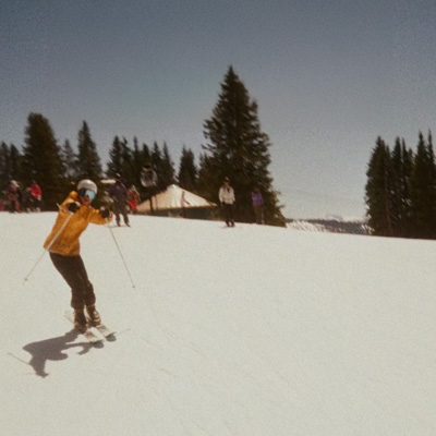 A snapshot photo of a skier on a flat snowy field with pine trees in the background