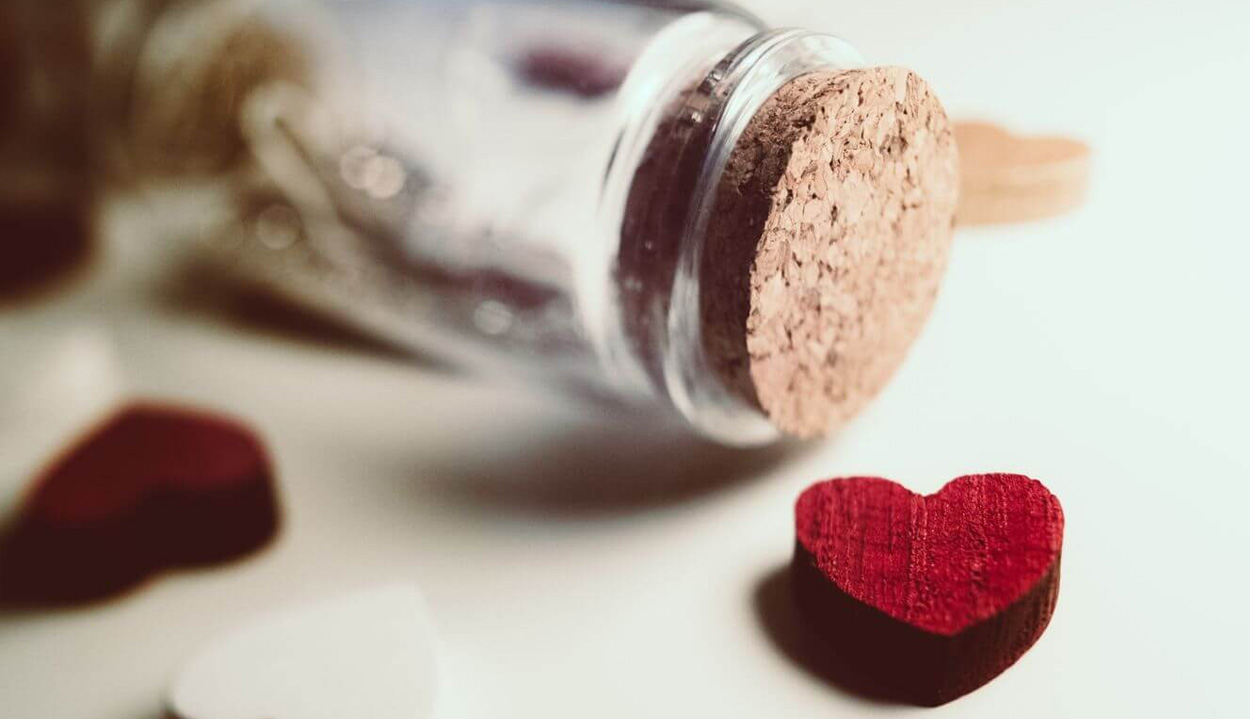 Close up of the top of a wine bottle and cork on lying horizontally on a surface with wooden red heart in the foreground