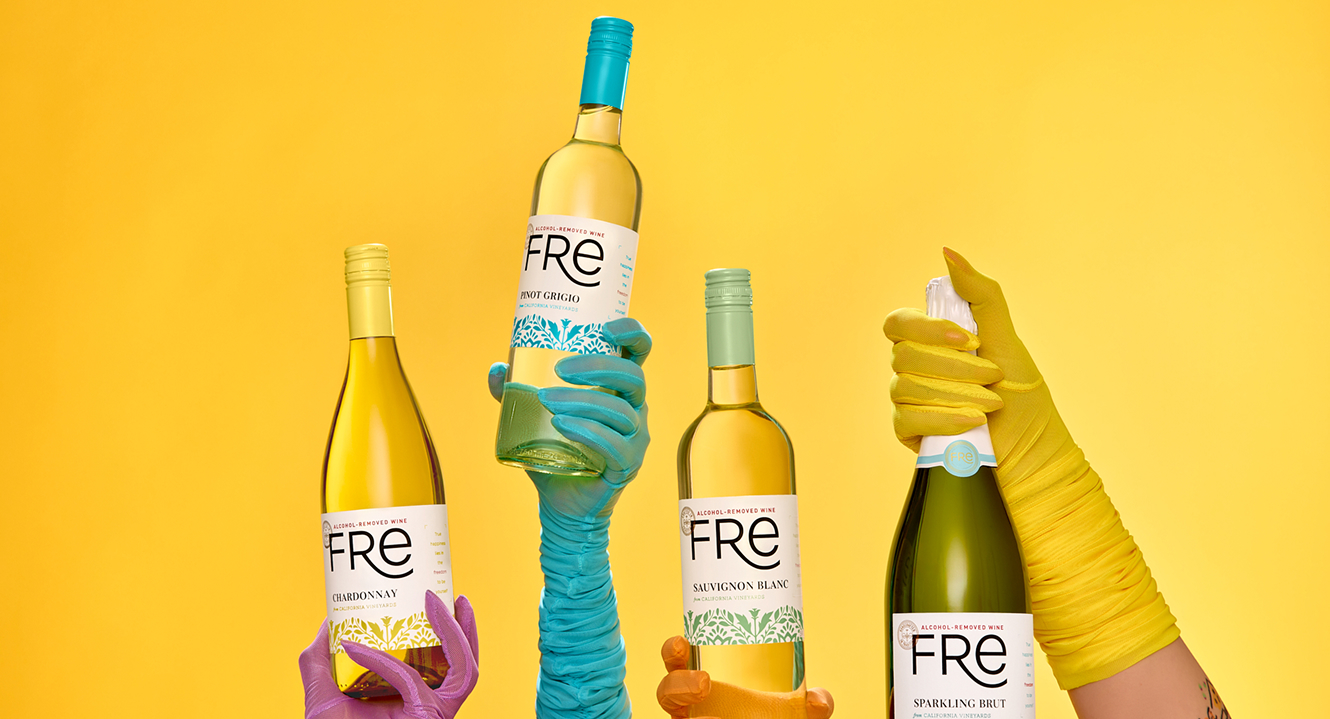 Hands wearing long evening wear-type gloves in bright colors hold various bottles of white Fre non-alcoholic wines in front of a solid yellow background