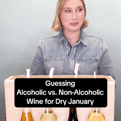 Top portion of a woman behind a barrier looking to the side, with an overlay caption in front of the barrier that reads "Guessing Alcoholic vs. Non-Alcoholic Wine for Dry January"