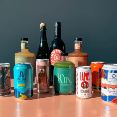 A grouping of products consisting of bottles and cans on a peach colored surface and dark blue gray background