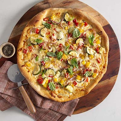 Bird's eye view of a small vegetable pizza on a wooden turret with a pizza cutter and cloth napkin