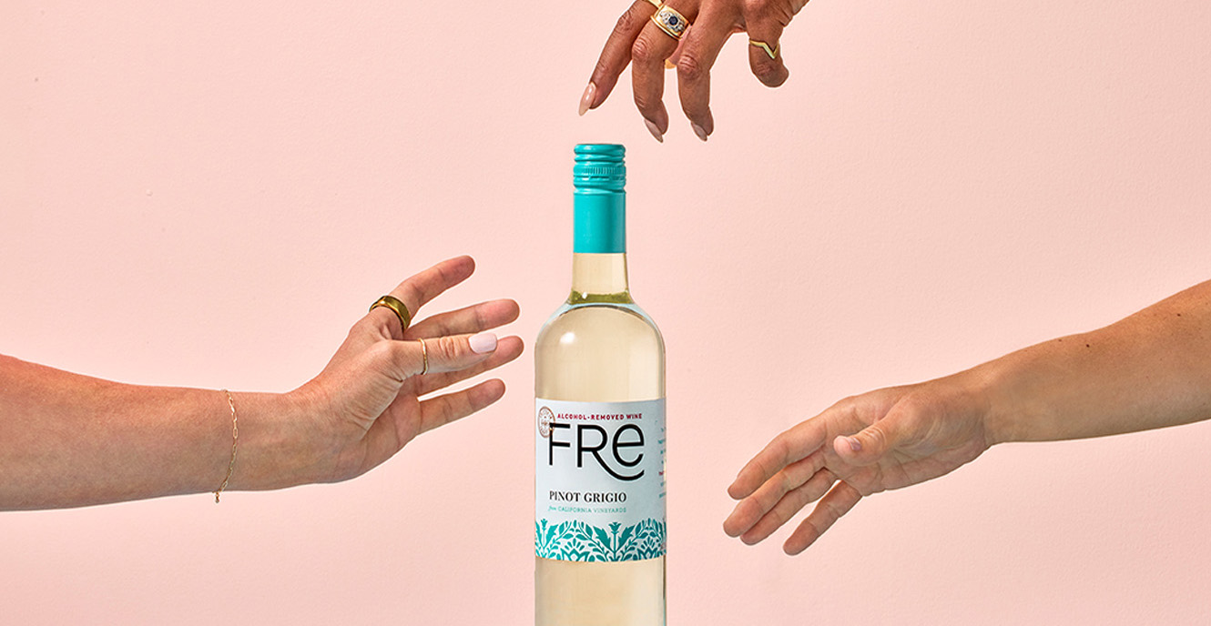 Three separate hands reaching for a bottle of Fre Alcohol-Removed pinot grigio white wine