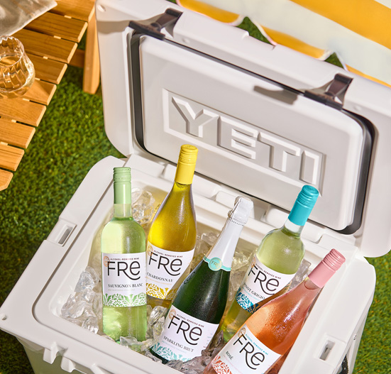 View from above in an outdoor setting of a Yeti cooler filled with ice with bottles of FRE wines nestled in the ice, on a grass surface, with a picnic table in the background